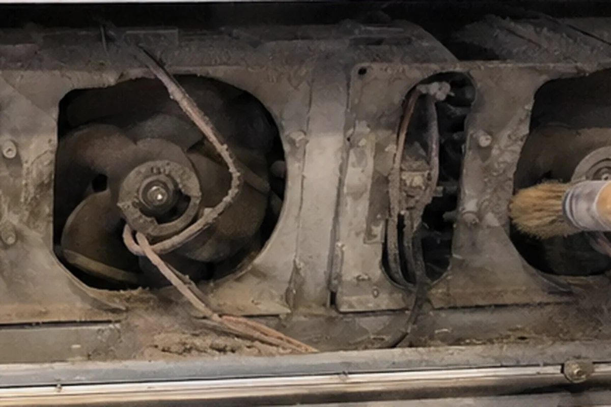 A blower wheel and its housing seen up close, the metal furred with grey deposit and the wiring loom running past it