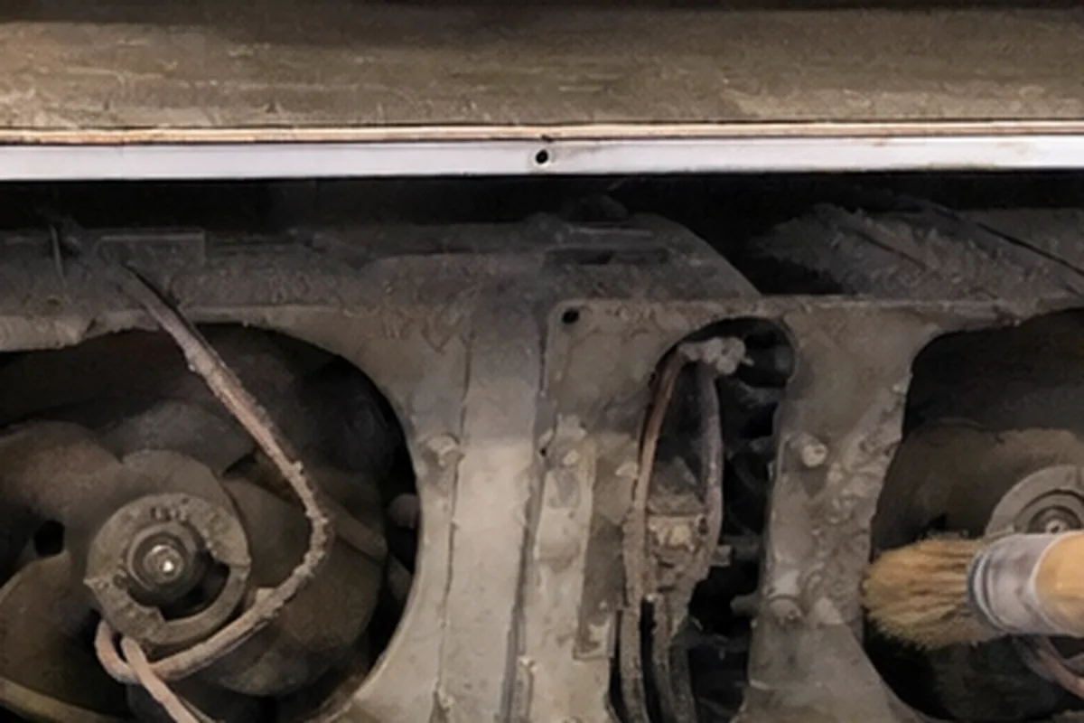 A brush working dust out from between the blades of an appliance cooling fan, the coil beside it half cleaned