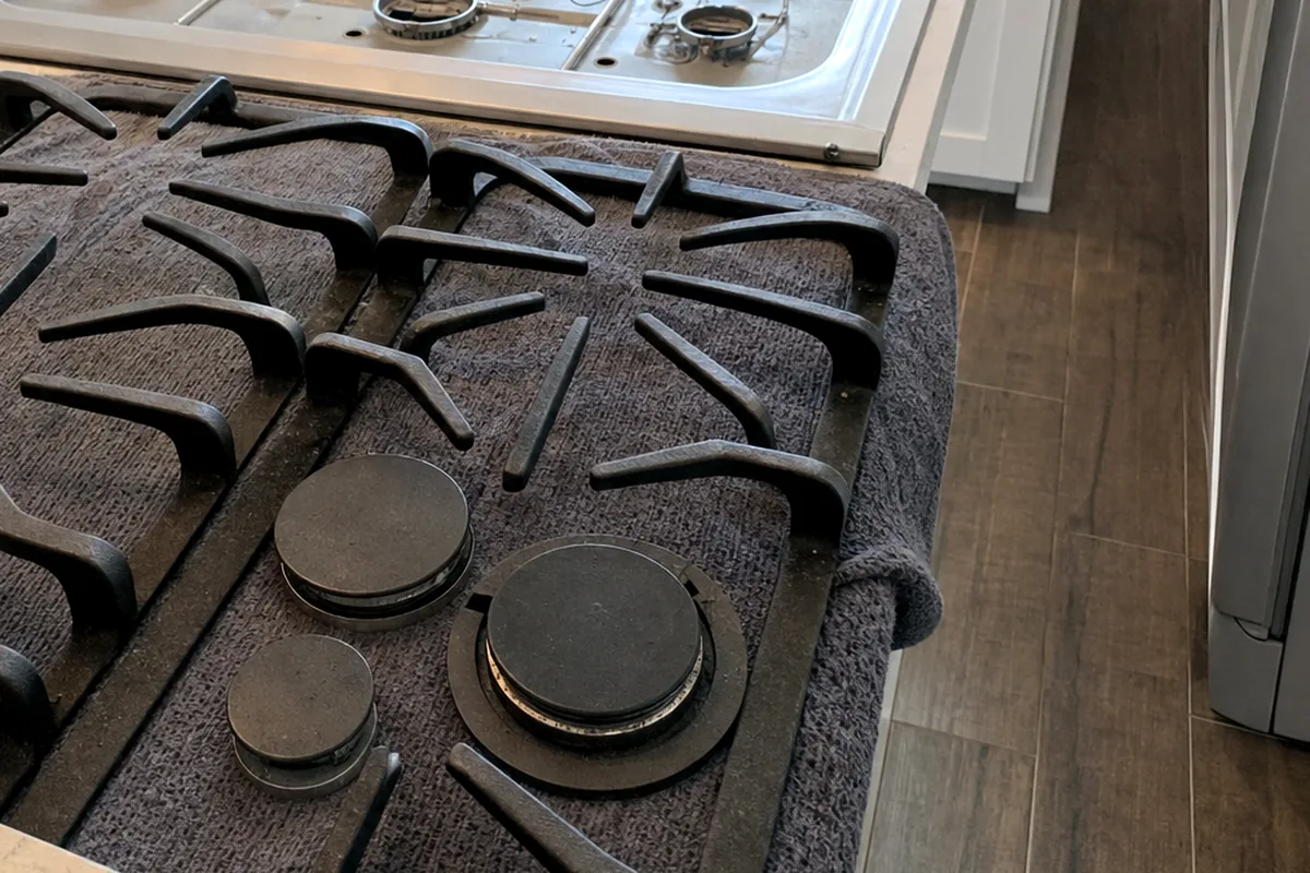 A gas rangetop mid-service, grates off, the burner heads and the stainless deck between them clearly lit