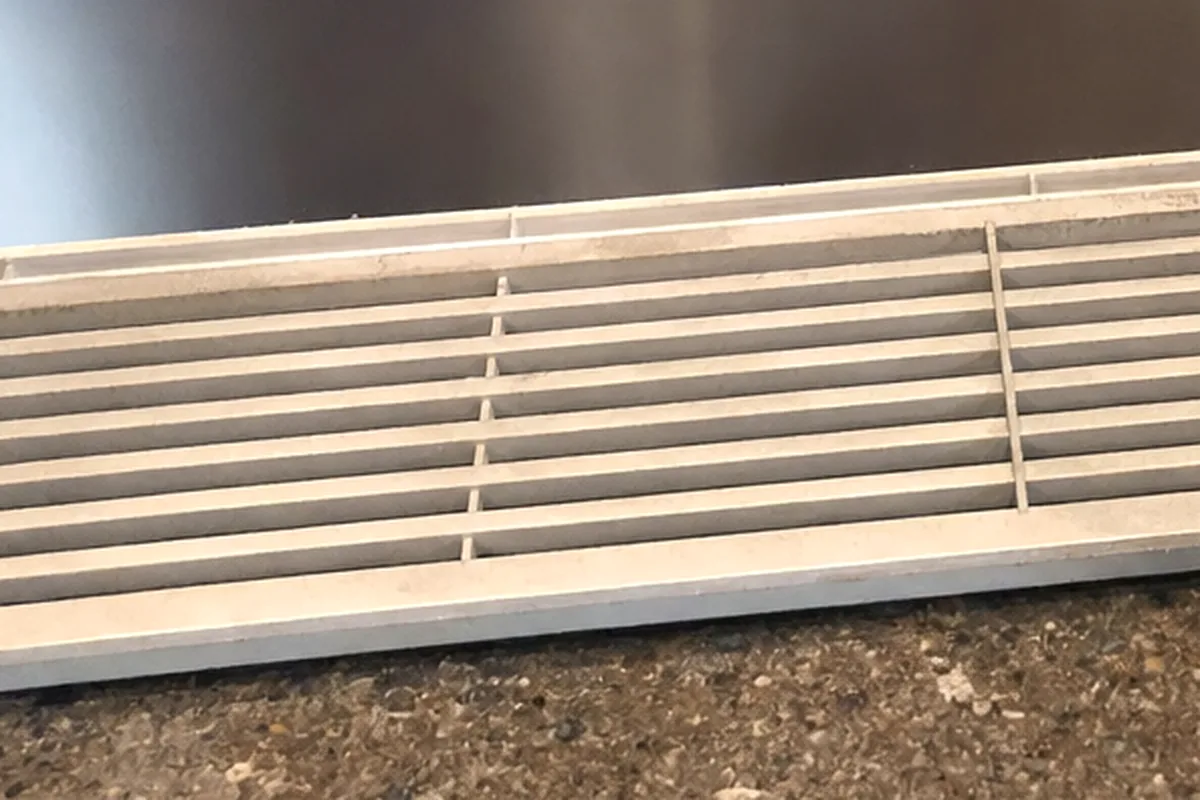 A removed stainless vent panel standing on the floor beside the tools used to take it off