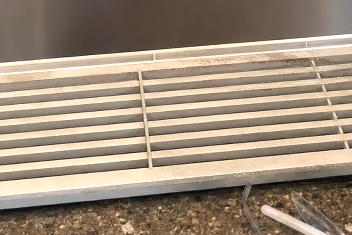 A long stainless louvred grille lifted off and leaned against the cabinet it came from